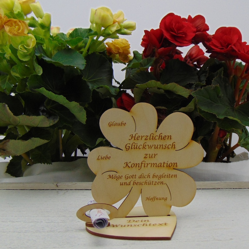 Op de afbeelding: Houten klavertje vier kaart met de tekst "Herzlichen Gl&uuml;ckwunsch zur Konfirmation" en "M&ouml;ge Gott dich begleiten und besch&uuml;tzen." De kaart is versierd met een hartvormige basis en een rol voor een gepersonaliseerd bericht.