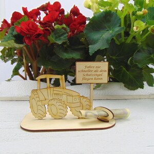 May include: Wooden tractor with a sign that reads "Fahre nie schneller als dein Schutzengel fliegen kann" and a rolled up bill of money.