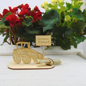 May include: Wooden tractor money holder with a sign that reads "For your wish". The tractor is brown and has a rolled up bill of money in the back.