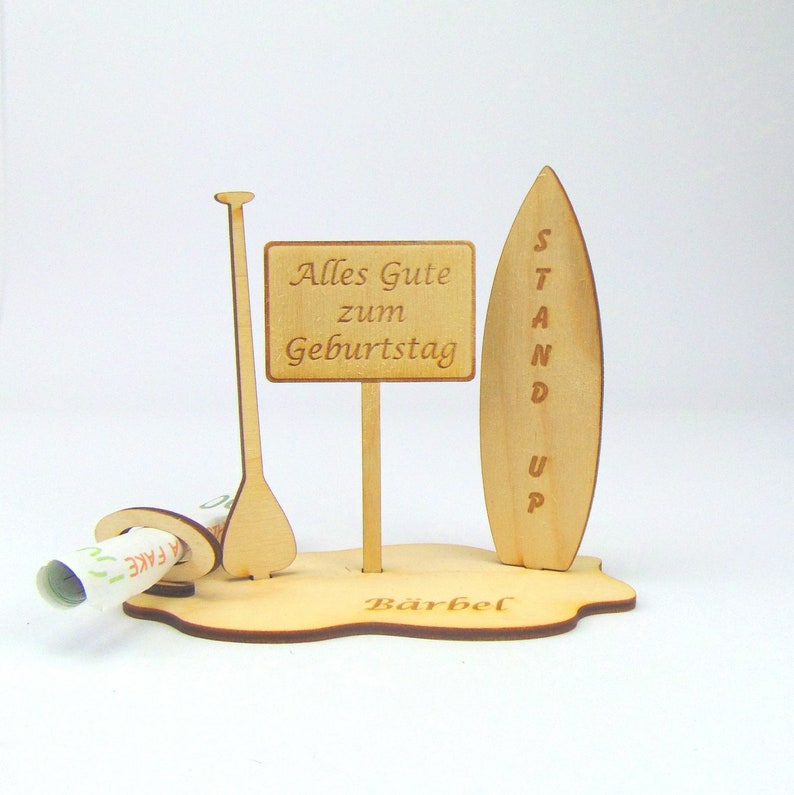 May include: Wooden stand up paddle board with a sign that says "Alles Gute zum Geburtstag" and the name "Barbel" on the base.