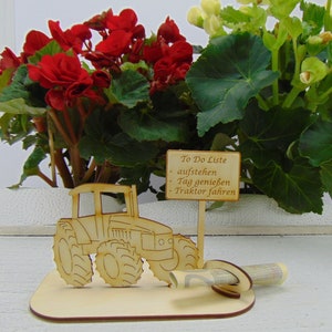 May include: Wooden tractor figurine with a sign that reads "To Do Liste - aufstehen - Tag geniessen - Traktor fahren". The figurine is on a wooden base with a rolled up bill of money.