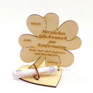 Op de afbeelding: Houten klavertje vier kaart met de tekst "Herzlichen Gl&uuml;ckwunsch zur Konfirmation" en "M&ouml;ge Gott dich begleiten und besch&uuml;tzen." De kaart heeft een gleuf voor een opgerold biljet en een hartvormige basis.