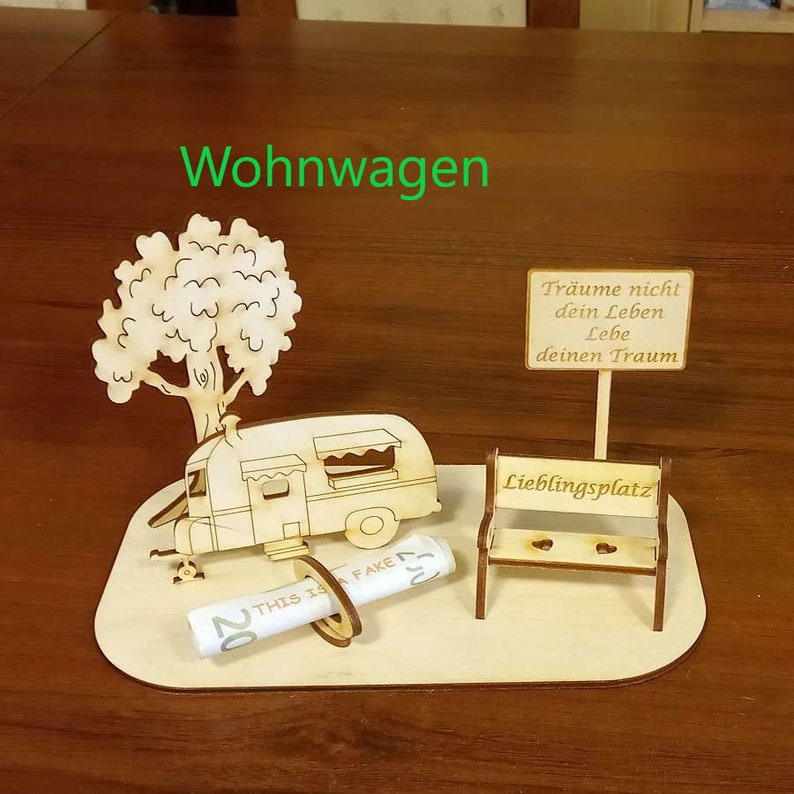 May include: A wooden model of a camper van, a tree, a bench, and a sign with the text "Tr&auml;ume nicht dein Leben Lebe deinen Traum" and "Lieblingsplatz". The model is on a wooden base.
