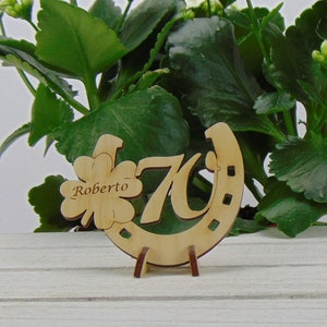 May include: Wooden horseshoe with the number 70 and a four-leaf clover with the name Roberto engraved on it. The horseshoe is on a small wooden stand.