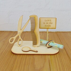 Puede incluir: Soporte de madera con un peine, tijeras, un espejo peque&ntilde;o y un letrero que dice "LOVE is in the HAIR".