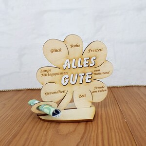 May include: A wooden clover-shaped sign with the words "Alles Gute" in the center. The sign has different wishes written on each leaf, such as "Gl&uuml;ck", "Ruhe", "Freizeit", "Lange Mittagspausen", "Gesundheit", "Zeit", "Freude am Leben", and "zum Ruhestand".