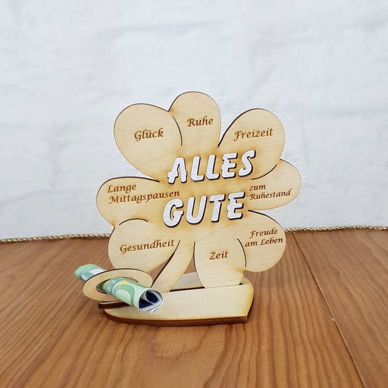 May include: A wooden clover-shaped sign with the words "Alles Gute" in the center. The sign has different wishes written on each leaf, such as "Gl&uuml;ck", "Ruhe", "Freizeit", "Lange Mittagspausen", "Gesundheit", "Zeit", "Freude am Leben", and "zum Ruhestand".