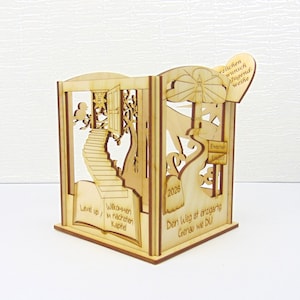 Op de afbeelding: Een lasergesneden houten doos met ingewikkelde ontwerpen. De doos heeft een trap, een deur en de tekst "Level up / nächsten Kapitel" en "Den Weg ist einzigartig Genau wie DU". Het jaar "2026" is ook zichtbaar.