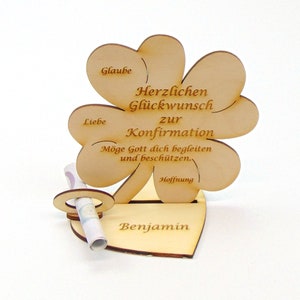 Op de afbeelding: Houten klavertje vier-kaarthouder met de tekst "Herzlichen Gl&uuml;ckwunsch zur Konfirmation" en "M&ouml;ge Gott dich begleiten und besch&uuml;tzen." De kaarthouder heeft een gleuf voor een opgerold biljet en een hartvormige basis met de naam "Benjamin" erop gegraveerd.