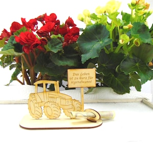 May include: Wooden tractor money holder with a sign that reads "Das Leben ist zu kurz f&uuml;r irgendwann!"  The tractor is brown and the sign is white with black lettering. The money holder is sitting on a wooden base.