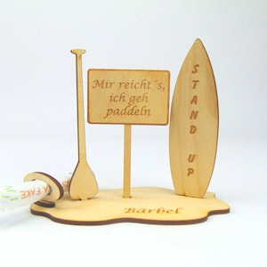 May include: Wooden stand up paddle board with a paddle and a sign that reads "Mir reicht's, ich geh paddeln" and the name "B&auml;rbel" at the bottom.