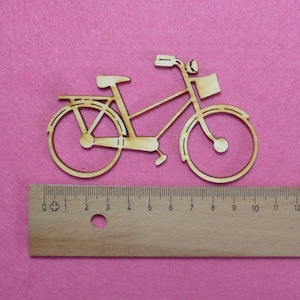 Könnte beinhalten: Holz-Fahrrad-Ausschnitt mit hellbraunem Finish. Das Fahrrad hat einen Korb, einen Sitz und einen Gepäckträger. Ein Holzlineal ist darunter platziert. Das Fahrrad misst etwa 15 cm in der Länge.