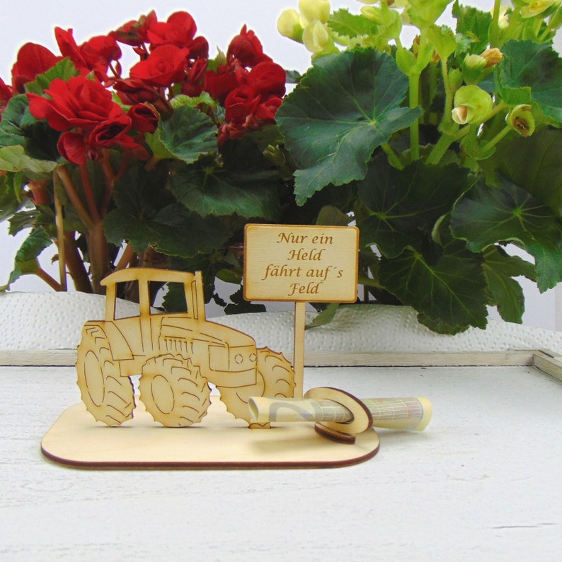 May include: Wooden tractor money holder with a sign that reads "Nur ein Held f&auml;hrt auf's Feld". The tractor is brown and has a green money slot. The sign is brown and has white text.