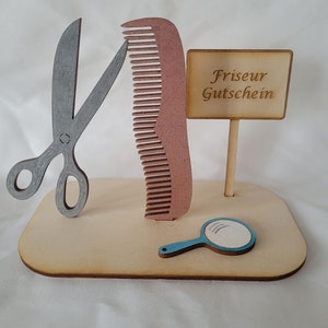 Puede incluir: Un soporte de madera con un par de tijeras plateadas, un peine marr&oacute;n, un espejo de mano azul y un cartel que dice "Friseur Gutschein".