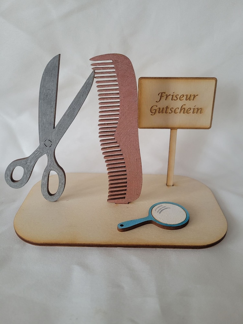 Puede incluir: Un soporte de madera con un par de tijeras plateadas, un peine marr&oacute;n, un espejo de mano azul y un cartel que dice "Friseur Gutschein".