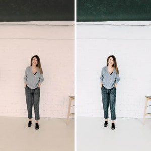 May include: A woman wearing a gray sweater and plaid pants stands in front of a white wall. She is smiling and has her hands in her pockets.