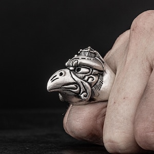 Puede incluir: Un anillo de plata con un diseño detallado de la cabeza de un pájaro con una corona en la parte superior.