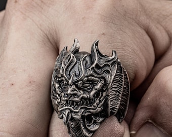 May include: A silver ring with a detailed design of a demon's face with horns and flames.