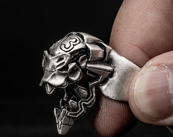 May include: A silver ring with a detailed design of a robot head. The robot head has a number "3" on the top.