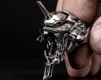 May include: A silver ring featuring a detailed, three-dimensional design of a robot head with an open mouth.