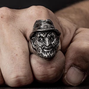 May include: A silver ring featuring a detailed sculpture of a horror movie character's head wearing a hat.