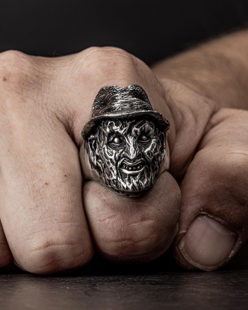 May include: A silver ring featuring a detailed sculpture of a horror movie character's head wearing a hat.