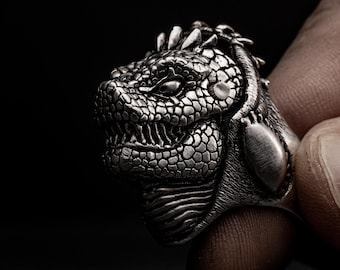 May include: A silver ring with a detailed design of a dragon's head. The ring is worn on a finger.