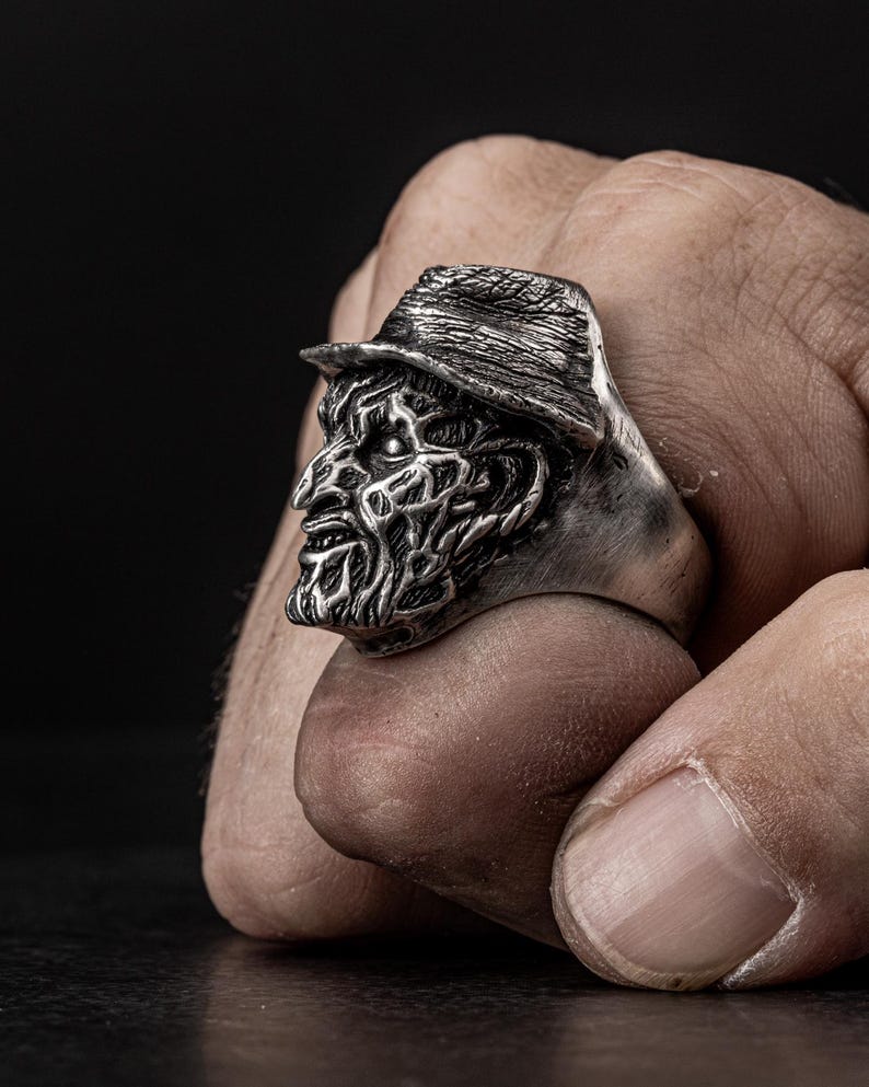 May include: A silver ring featuring a detailed, three-dimensional sculpture of a horror movie character's head wearing a hat.
