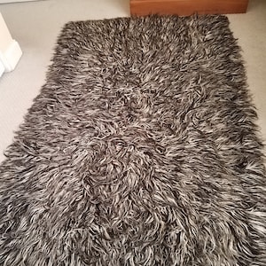 Könnte beinhalten: Ein flauschiger, langhaariger Teppich in Schwarz-Weiß. Der Teppich ist aus einem weichen, plüschigen Material gefertigt und hat eine zottelige Textur.