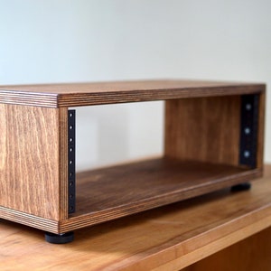 May include: A wooden rack for audio equipment with black metal rails. The rack has a natural wood finish and sits on four black rubber feet.