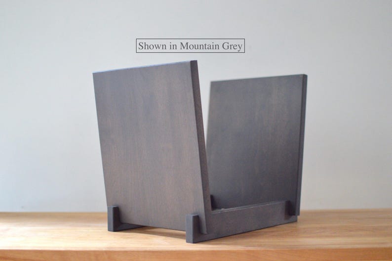 May include: A mountain grey wooden record storage crate with two vertical side panels and a base support. The text "Shown in Mountain Grey" is printed above the object. The structure is composed of flat, rectangular wooden pieces joined together.
