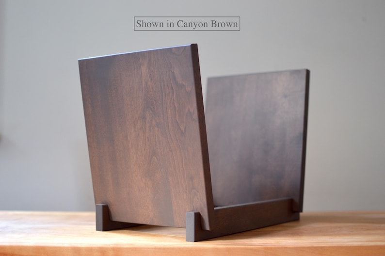 May include: A dark brown wooden record storage crate with a smooth finish and visible wood grain. The structure consists of two upright side panels connected by a base. The text "Shown in Canyon Brown" is printed at the top center.