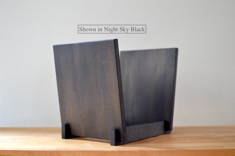 May include: A dark wood record storage crate with a flat base and two upright side panels. The wood features a visible grain pattern in a deep black finish. A rectangular label above the crate contains the text Shown in Night Sky Black.