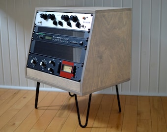 Puede incluir: Un soporte de madera con patas de metal negro, que sostiene una consola de mezcla de audio vintage con perillas, botones y un medidor.
