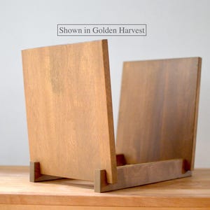 May include: A wooden record storage stand with two upright panels and a base, featuring a medium brown finish. The text "Shown in Golden Harvest" is printed in a rectangular box above the stand, indicating the color of the wood grain.