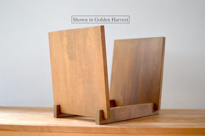 May include: A wooden record storage stand with two upright panels and a base, featuring a medium brown finish. The text "Shown in Golden Harvest" is printed in a rectangular box above the stand, indicating the color of the wood grain.