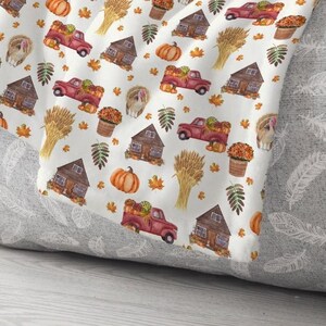 May include: A white throw blanket featuring a repeating watercolor pattern of red pickup trucks carrying pumpkins, brown wooden cabins, golden wheat sheaves, orange pumpkins, potted autumn flowers, turkeys, and scattered colorful fall leaves.