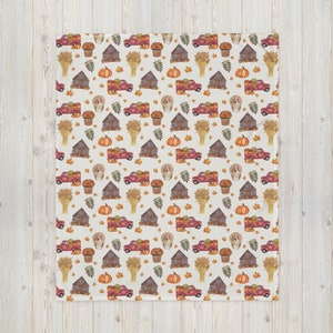 May include: A white throw blanket featuring a repeating watercolor pattern of red pickup trucks carrying pumpkins, brown rustic cabins, orange pumpkins, golden wheat sheaves, turkeys, potted orange flowers, and scattered autumn leaves.