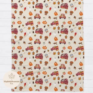 May include: A cream-colored blanket featuring a repeating pattern of red barns, red pickup trucks carrying pumpkins, orange pumpkins, white pumpkins, brown acorns, pinecones, autumn leaves, cinnamon sticks, and coffee cups with the Maple&Mountain Co. logo.