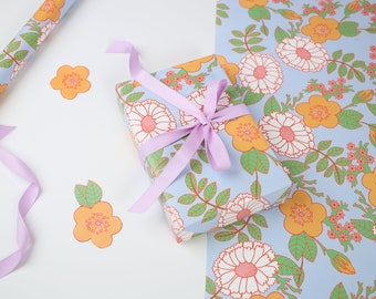 May include: A gift wrapped in blue floral wrapping paper with a light purple ribbon. The wrapping paper features a pattern of white and orange flowers with green leaves.