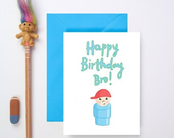 May include: A white card with a blue envelope. The card has a green and blue illustration of a boy with a red hat and the text "Happy Birthday Bro!"