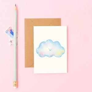 Może przedstawiać: Kartka okolicznościowa z akwarelową ilustracją chmury w odcieniach niebieskiego, różowego i żółtego, z uśmiechniętą twarzą. Obraz zawiera brązową kopertę, jasnozielony ołówek i znaczki pocztowe, wszystko na różowym tle.