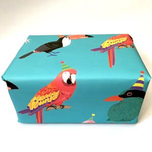 May include: Blue wrapping paper with a repeating pattern of colourful parrots wearing party hats. The parrots are a toucan, a macaw, and a green bird.