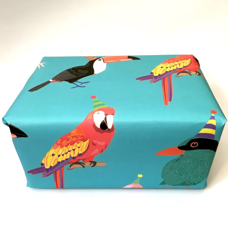 May include: Blue wrapping paper with a repeating pattern of colourful parrots wearing party hats. The parrots are a toucan, a macaw, and a green bird.