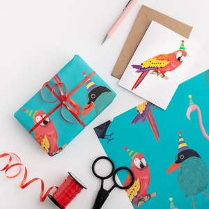 May include: A blue gift box with a red ribbon and a parrot design. The box is surrounded by red curling ribbon, a spool of red ribbon, a pair of scissors, and a card with a parrot design.