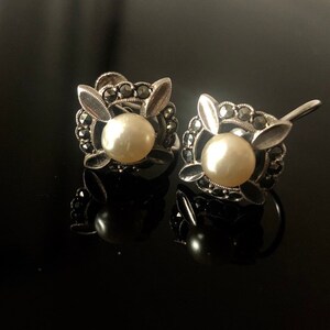 May include: A pair of silver earrings with a pearl and marcasite stones in a floral design.