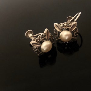 May include: A pair of silver earrings with a pearl and marcasite stones. The earrings have a clip-on closure.