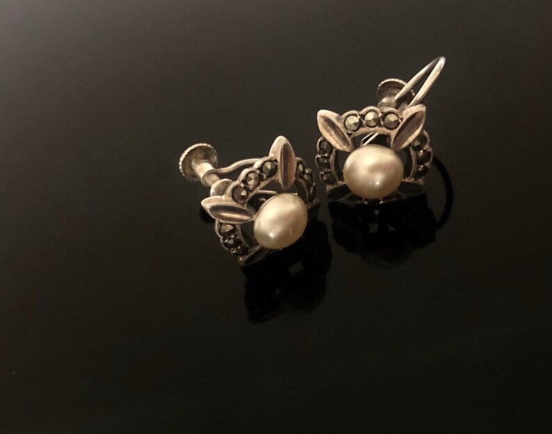 May include: A pair of silver earrings with a pearl and marcasite stones. The earrings have a clip-on closure.