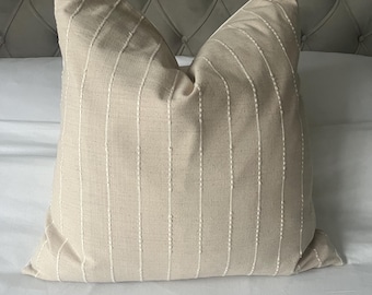 May include: A beige throw pillow with white vertical stripes. The pillow is made of a soft, textured fabric.