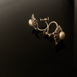 May include: A pair of silver clip-on earrings with a pearl and marcasite design.